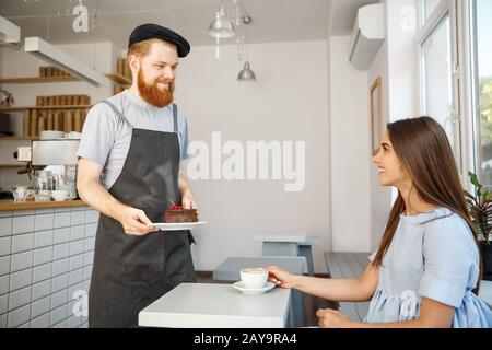 Kaffee-Business-Konzept - Kellner oder Barkeeper, der Schokoladenkuchen gibt und mit der kaukasischen schönen Dame in blauem Kleid bei C spricht Stockfoto