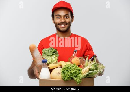 Lieferkonzept - Ein Gutaussehender afroamerikanischer Liefermann, der eine Packung Lebensmittel und Getränke aus dem Geschäft mitführt. Isoliert ein Stockfoto