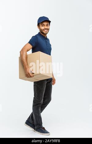 Lieferkonzept - Portrait Of Happy African American Delivery man in Blue Cloth Walking, um dem Kunden ein Paketpaket zu schicken. Isol Stockfoto