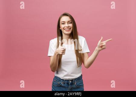 Foto der glückliche junge Frau stehen und poiting Finger über rosa Hintergrund isoliert. Stockfoto