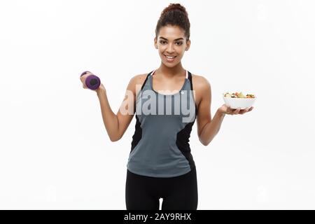 Healthy and Fitness-Konzept - Schöne sportive afroamerikanische Ernährung mit Hanteln und frischem Salat an den Händen. Isoliert auf w Stockfoto