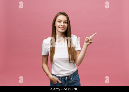 Foto der glückliche junge Frau stehen und poiting Finger über rosa Hintergrund isoliert. Stockfoto