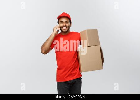 Lieferkonzept - Portrait des Ansehnlichen afroamerikanischen Lieferers oder Kurierers mit Telefon-Box an den Kunden. Isoliert ein Stockfoto