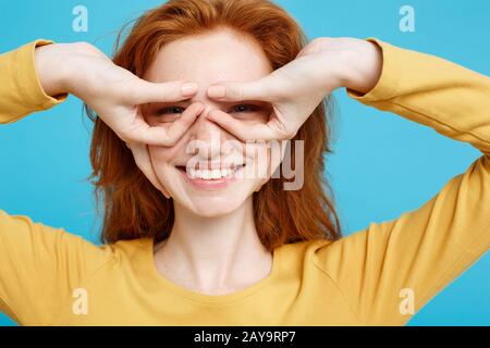 Fun and People Konzept - Headshot Portrait of Happy Ingwer Red Hair Girl with freckles Smiling and Making Finger Glasses. Pastell Stockfoto