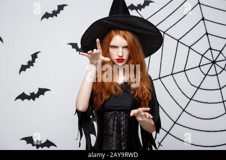 Halloween Witch Concept - Halloween Witch in Voller Länge Zaubersprüche mit ernsthaftem Ausdruck über dunkelgrauem Studiohintergrund Wi Stockfoto