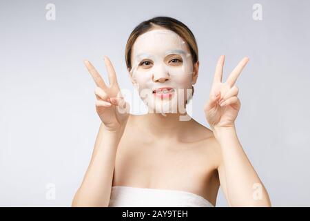Schöne asiatische Frau Anwendung Blatt Papier Maske auf dem Gesicht weißen Hintergrund. Stockfoto