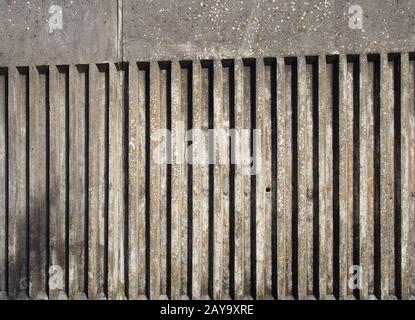 Alte Betonaußenwand mit geriffeltem, vertikalem Streifendesign mit rauer Gussstruktur und Schatten Stockfoto