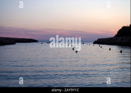 Die Bucht in der cala santandria in ciutadella in der Dämmerung mit einem leuchtenden violetten und rosafarbenen Abendhimmel Stockfoto