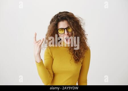 Schöne lustige, verblüffte Rockerin mit lockiger Frisur und stehen mit Rockabzeichen und Blick auf die Kamera. Studio Shot, isoliert Stockfoto