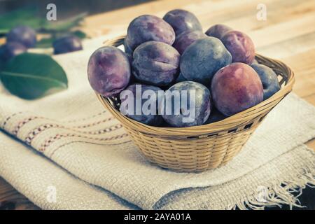 Große reife Pflaumen in einem Weidenkorb. Stockfoto