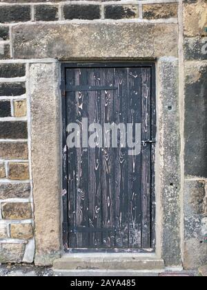 Alte schwarze Holztür mit alter verblichener Schälfarbe in einem schweren Steinrahmen Stockfoto