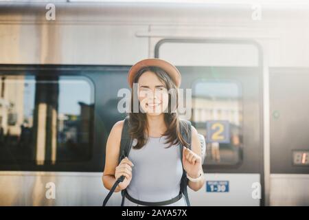 Themeneisenbahn und Reisen. Portrait junge kaukasische Frau mit tollem Lächeln im Hintergrund des Bahnhofs mit Backp Stockfoto