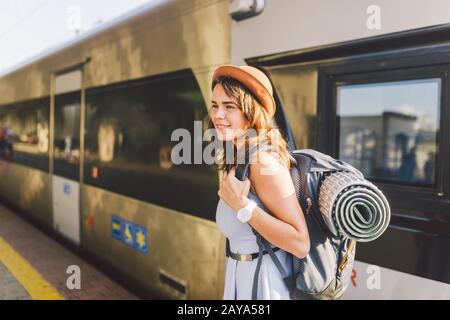 Themeneisenbahn und Reisen. Portrait junge kaukasische Frau mit tollem Lächeln im Hintergrund des Bahnhofs mit Backp Stockfoto