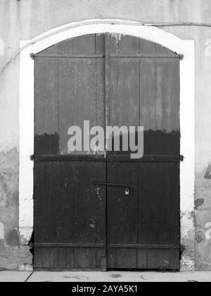 Monochromes Bild alter geschlossener Holztüren auf einem leeren derben Haus mit ungleichmäßiger Farbe Stockfoto