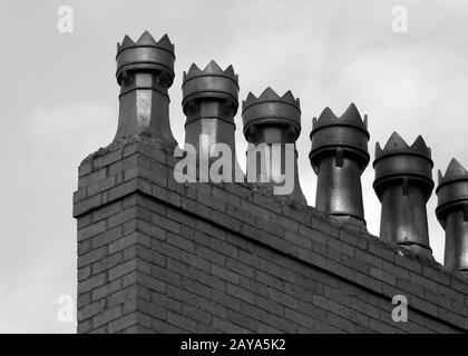 Monochromes Bild eines reihigen, altmodischen Kamintöpfen auf einem aus Backstein erbauten Haus Stockfoto