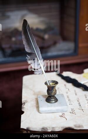 Alter Quillenstift, Bücher und Vintage-Inkwell auf Holzpult im alten Büro vor dem Hintergrund des Bücherregals und der Strahlen von Stockfoto