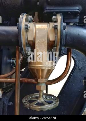 Großes altes Messingindustrieventil mit Rundgriff auf einer großen schwarzen Maschine mit Kupferrohr montiert Stockfoto