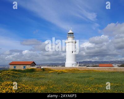 Der alte Leuchtturm in paphos, zypern, umgeben von historischen Gebäuden mit Frühlingsblumen, die an einem Weg zum wachsen Stockfoto