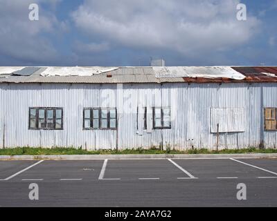 Ein altes verlassenes weißes Industriegebäude mit rostendem gepatschtem, repariertem Welldach und mit Fenstern Stockfoto