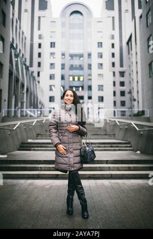 Porträt einer Frau zu einem geschäftlichen Thema. Junges kaukasisches brünette Mädchen in langer Jacke, Mantel mit schwarzer Ledertasche steht im Bus Stockfoto