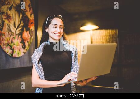 Das Konzept von Kleinunternehmen und Technologie. Junge schöne Brunette-Geschäftsfrau in schwarzem Kleid und grauem Pullover steht in c Stockfoto