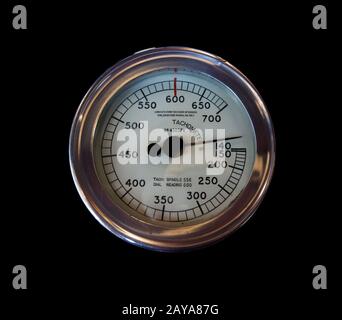 Ein alter industrieller Rundmetalltachometer auf schwarzem Hintergrund mit Zahlen, die auf einem weißen Ziffernblatt markiert sind Stockfoto