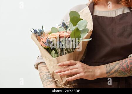 Frische Blumen leben Korallenrosen und Eryngium als Glückwunsch Bouquet in der Hand des Mädchens mit Tattoo, Kopier Raum. Postkarte für Mo Stockfoto