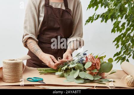 Blumenfrau kreist frischen Rosenstrauß auf grauem Hintergrund. Schritt für Schritt verarbeiten. Kleine Unternehmen mit Blumenlieferung. M Stockfoto