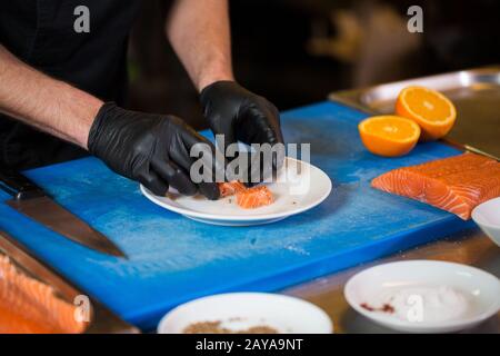 Themenkochen ist ein Beruf des Kochens. Nahaufnahme der Hand eines kaukasischen Mannes in einer Restaurantküche, in der rote Fischfilets zubereitet werden Stockfoto