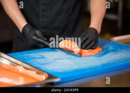 Themenkochen ist ein Beruf des Kochens. Nahaufnahme der Hand eines kaukasischen Mannes in einer Restaurantküche, in der rote Fischfilets zubereitet werden Stockfoto