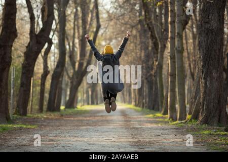 Aufgeregte junge Frau springt mit aufgezogenen Armen Stockfoto