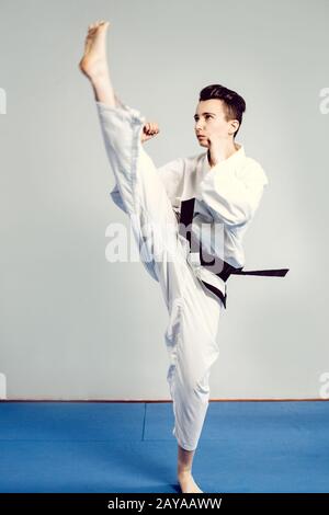 Mädchen im Karate Anzug Kimono im Studio mit grauem Hintergrund. Weibliches Kind zeigt Judo oder Karate stans in weißer Uniform mit schwarzem bel Stockfoto