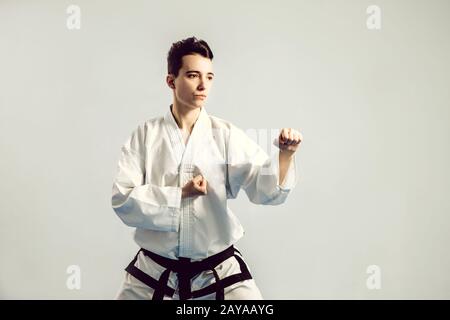 Mädchen im Karate Anzug Kimono im Studio mit grauem Hintergrund. Weibliches Kind zeigt Judo oder Karate stans in weißer Uniform mit schwarzem bel Stockfoto