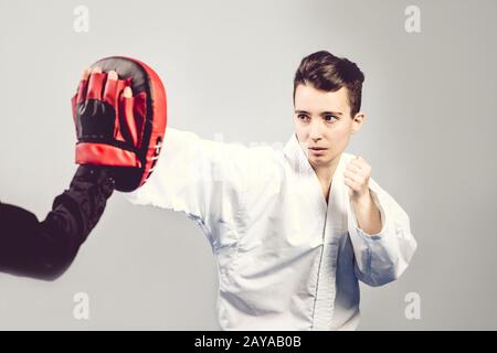 Mädchen im Karate Anzug Kimono im Studio mit grauem Hintergrund. Weibliches Kind zeigt Judo oder Karate stans in weißer Uniform mit schwarzem bel Stockfoto