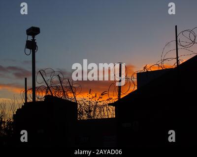 Stacheldraht und Sicherheitskamera auf einer Wand mit Abendhimmel und Sonnenuntergang Stockfoto