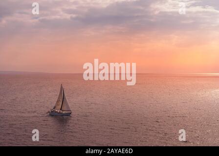 Lahaina, Maui, Hawaii, USA. - 12. Januar 2012: Kleines Segelboot auf rosafarbenem bis orangefarbenem Ozean unter rosafarbenem bis blauem Morgenhimmel. Stockfoto