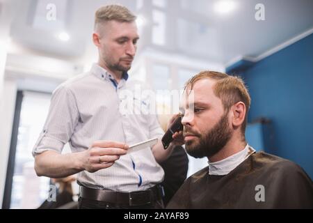 Nahaufnahme des Mannes, der im barber Shop trendige Frisur bekommt. Haarstylisten für Männer, die den Kunden bedienen und Haarschnitt mithilfe von Maschine und Co. Machen