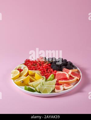 Satz von verschiedenen Zitrusfrüchten und Beeren in eine Platte auf einem rosa Hintergrund mit Kopie Raum vorgestellt. Gesunde Vitamin Essen Stockfoto