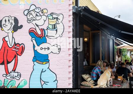 Byron Bay Cafe, Freunde treffen sich mit ihren Haustieren für den Morgenkaffee in Byron Bay Stadtzentrum, New South Wales, Australien Popeye und Ethel Illustration Stockfoto