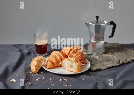 Frisch gebackene Croissants mit Kaffeetasse auf dunkelgrauem Hintergrund. Stockfoto