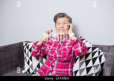 Theme Old Person verwendet Technologie. Reife Freude Lächeln aktiv graues Haar kaukasische Falten Frau sitzt zu Hause im Wohnzimmer o Stockfoto