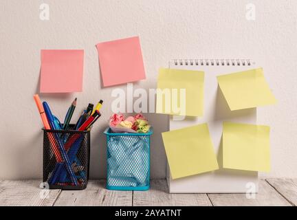 Neat Workplace mit 6 leeren farbigen Stick Pad Notes, die sowohl an der weißen Wand als auch an einem Open Spiral Notebook mit 2 vollen Bleistifttöpfen auf W platziert werden Stockfoto