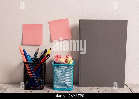 Gepflegter Arbeitsplatz mit leeren farbigen Stick-Pad-Notizen an der weißen Wand und zwei vollen Bleistifttöpfen und grauem Hardcover-Notizbuch an der Arbeit Stockfoto