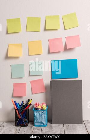 Gepflegter Arbeitsplatz mit 12 leeren farbigen Stick-Pad-Notizen und blauer Karte an der weißen Wand und 2 vollen Bleistifttöpfen neben Grey Hardcov Stockfoto