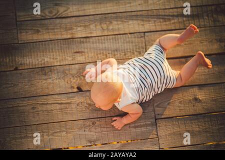 Neugeborenes Kind EIN Junge, ein Jahr alt, liegt auf dem Bauch auf einem Holzdock, einem Pier in gestreifter Kleidung, einem Draufsicht, einer Sommercom Stockfoto