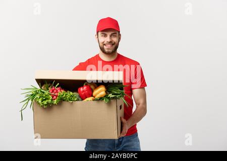 Lieferung Konzept: Stattlichen kaukasischen Lebensmittel-lieferservice Kurier Mann in der roten Uniform mit Lebensmittelgeschäft, mit frischem Obst und Gemüse Stockfoto