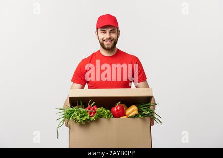 Lieferung Konzept: Stattlichen kaukasischen Lebensmittel-lieferservice Kurier Mann in der roten Uniform mit Lebensmittelgeschäft, mit frischem Obst und Gemüse Stockfoto