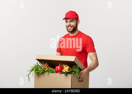 Lieferung Konzept: Stattlichen kaukasischen Lebensmittel-lieferservice Kurier Mann in der roten Uniform mit Lebensmittelgeschäft, mit frischem Obst und Gemüse Stockfoto