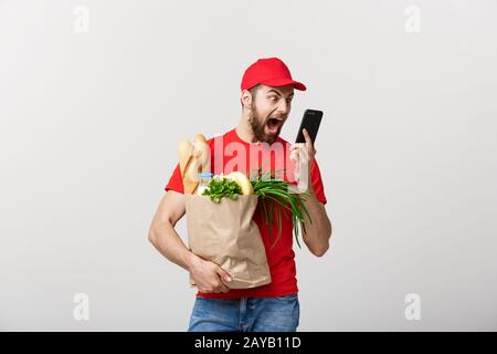 Lieferung Konzept: Stattlichen kaukasischen Lebensmittel-lieferservice Kurier Mann in der roten Uniform mit Lebensmittelgeschäft, mit frischem Obst und Gemüse Stockfoto