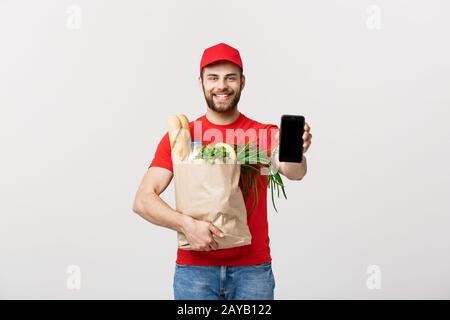 Lieferung Konzept: Stattlichen kaukasischen Lebensmittel-lieferservice Kurier Mann in der roten Uniform mit Lebensmittelgeschäft, mit frischem Obst und Gemüse Stockfoto